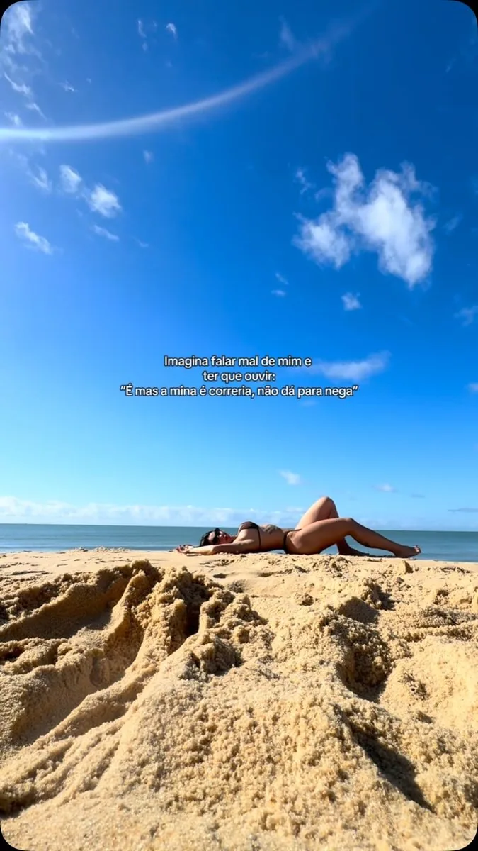 Anna Paulla Alves descansando na areia diante do mar em um dia de céu azul
